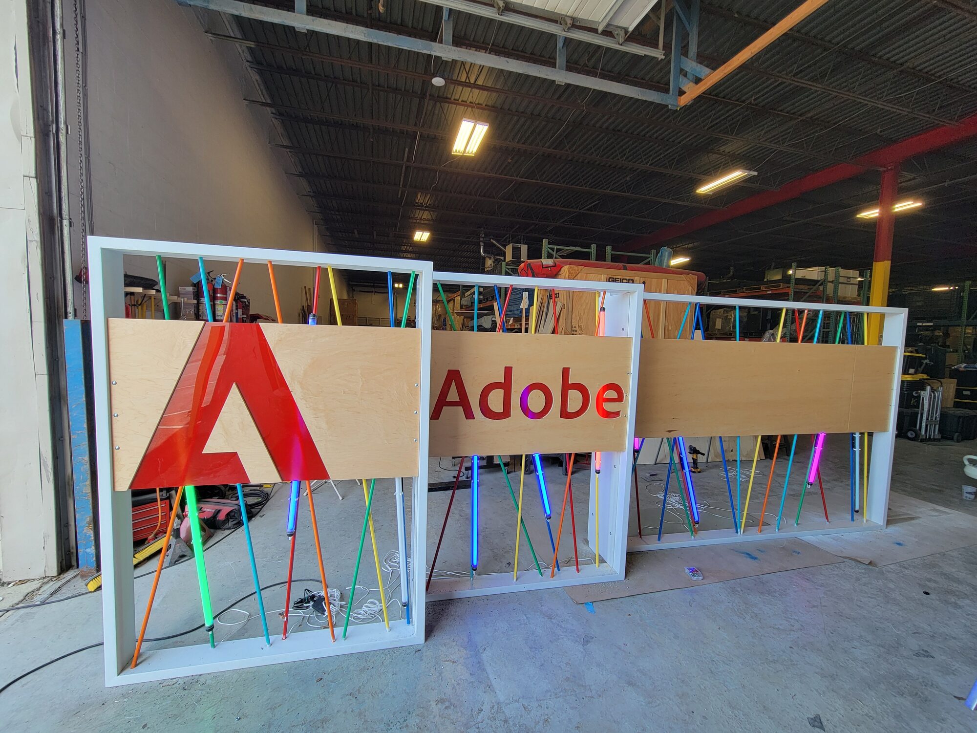Three assembled activation walls in the shop, red Adobe A mark and Adobe wordmark panels lit, conduit and LED bars glowing