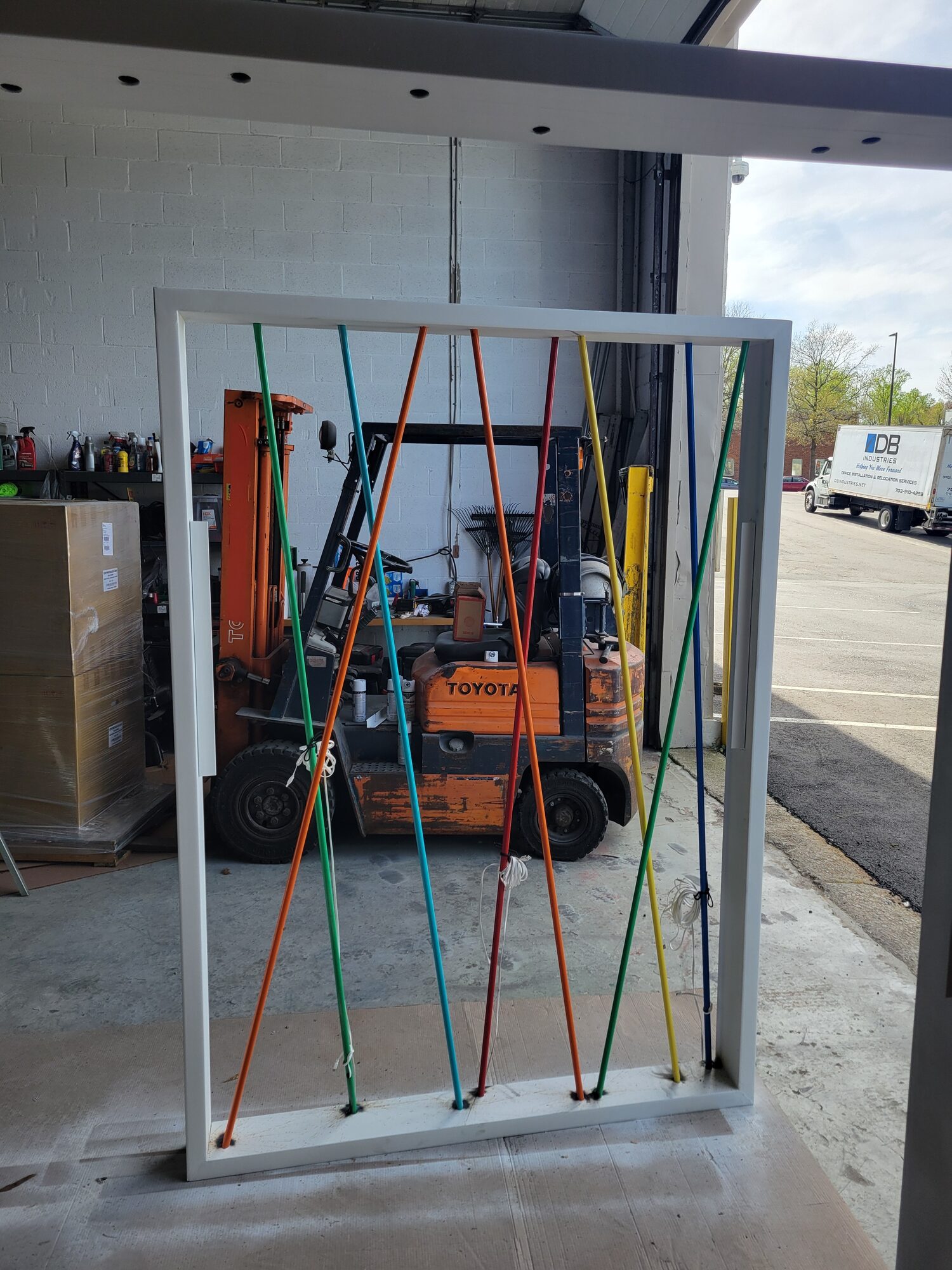 White steel wall frame outside the shop with 5 colors of steel conduit strung diagonally corner to corner