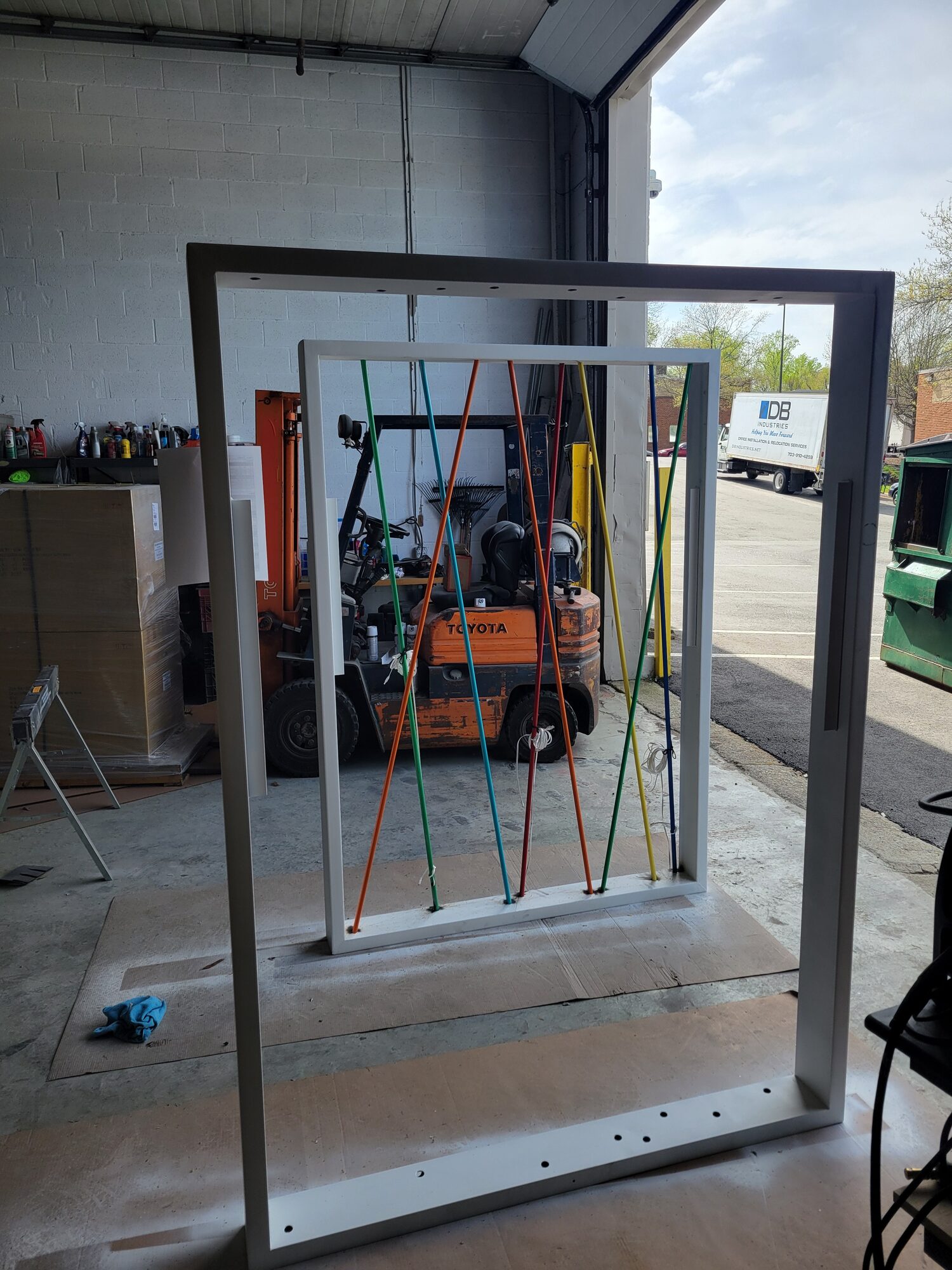 Two wall frames outside the shop, one with conduit fully strung and one still bare, showing the assembly sequence across the three matching walls
