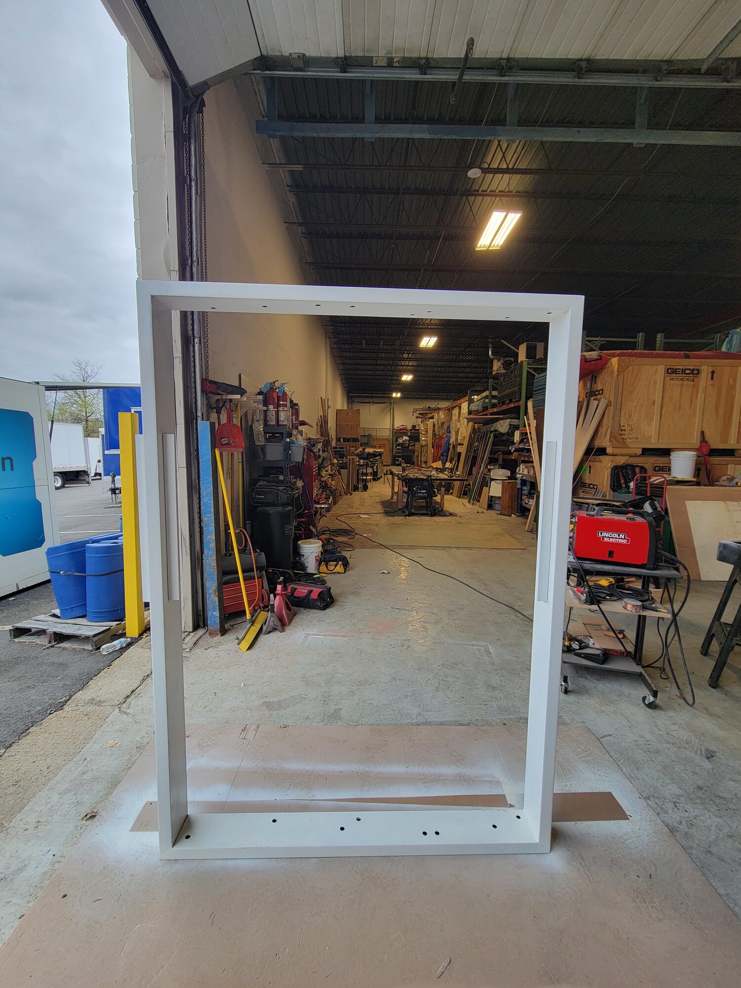 Welded and painted white steel wall frame standing in the shop doorway before conduit or panels are installed