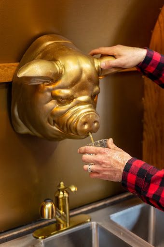 Photo of whiskey pouring from the gold pig-head spigot into a tasting glass